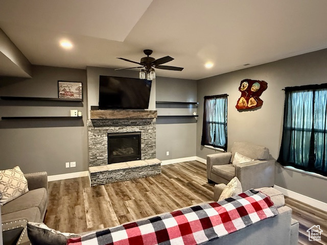 Living room with a ceiling fan, wood finished floors, a stone fireplace, and recessed lighting