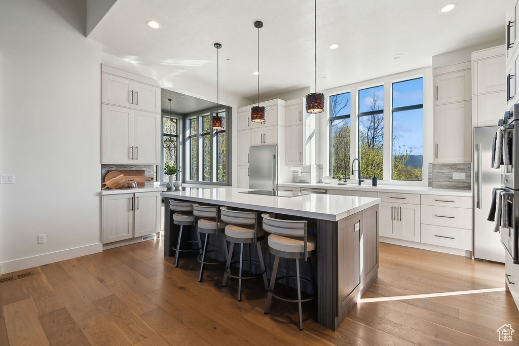 Kitchen with built in fridge, backsplash, recessed lighting, an island with sink, and light wood-style floors