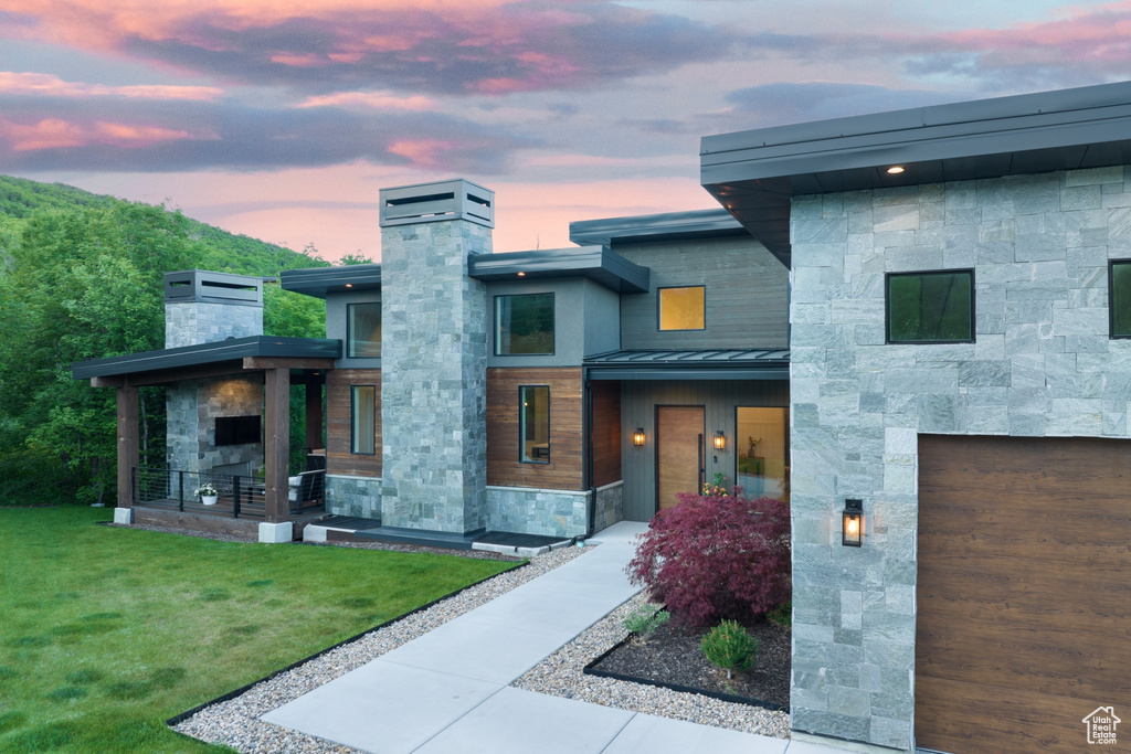 Modern home with a standing seam roof, a chimney, a front yard, stone siding, and a metal roof