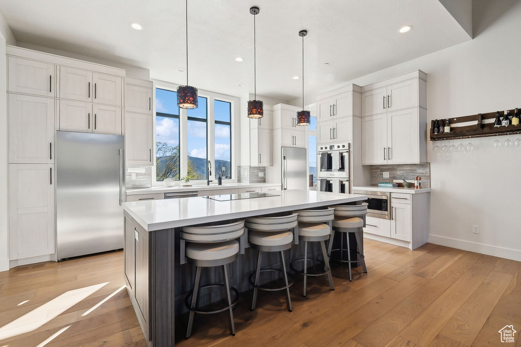 Kitchen with built in appliances, backsplash, light countertops, light wood-type flooring, and recessed lighting