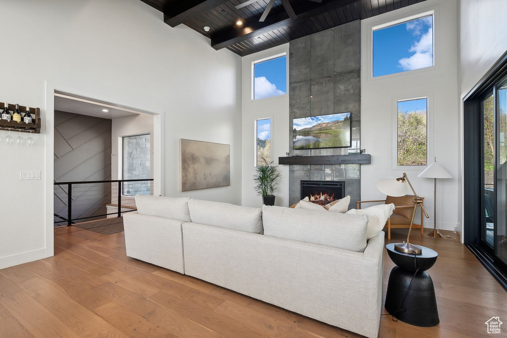 Living room featuring a towering ceiling, wood finished floors, plenty of natural light, a tile fireplace, and a wooden ceiling with exposed beams