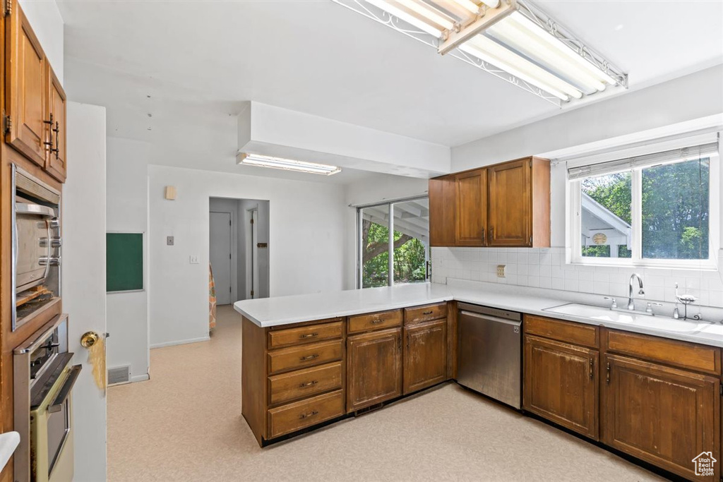Kitchen featuring appliances with stainless steel finishes, a peninsula, brown cabinetry, tasteful backsplash, and light countertops