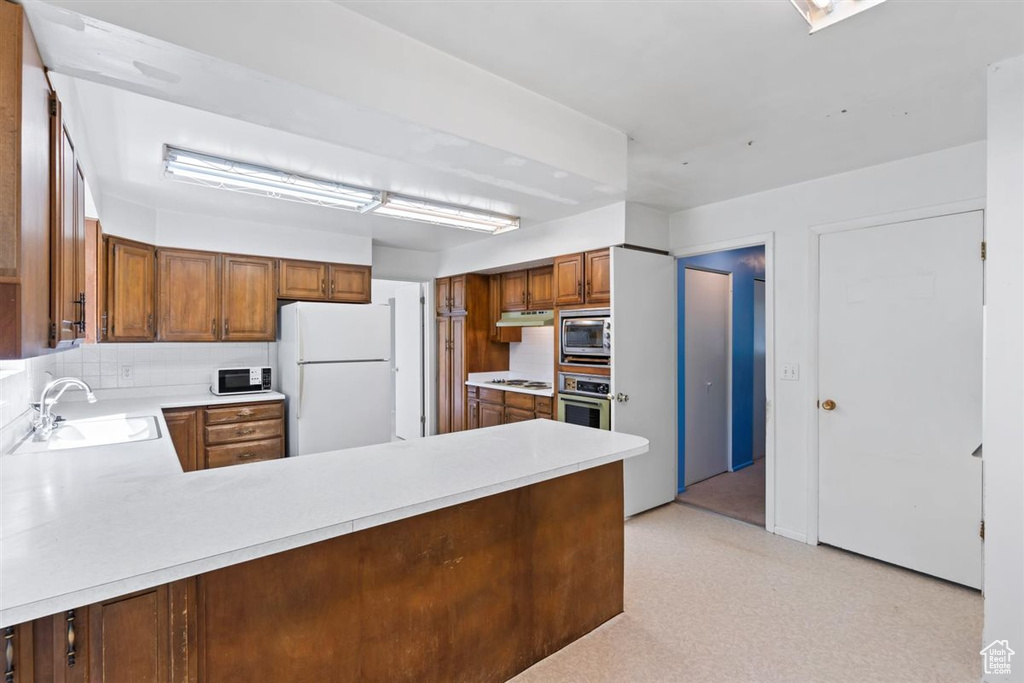 Kitchen featuring stainless steel appliances, light countertops, under cabinet range hood, a peninsula, and brown cabinetry
