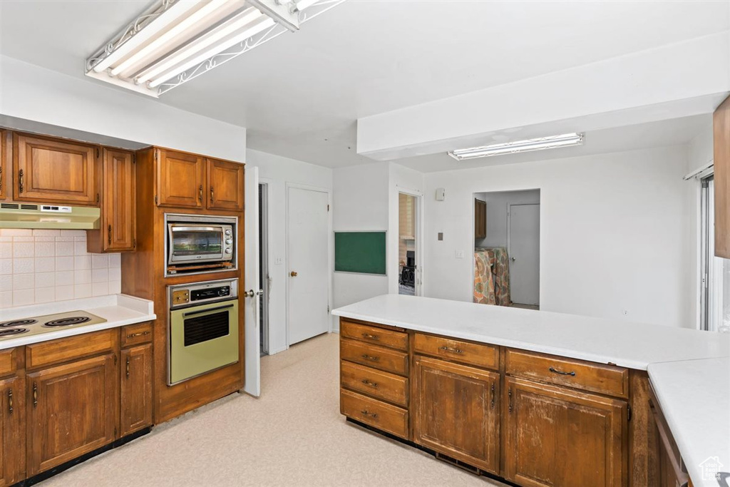 Kitchen with appliances with stainless steel finishes, under cabinet range hood, light countertops, backsplash, and brown cabinets