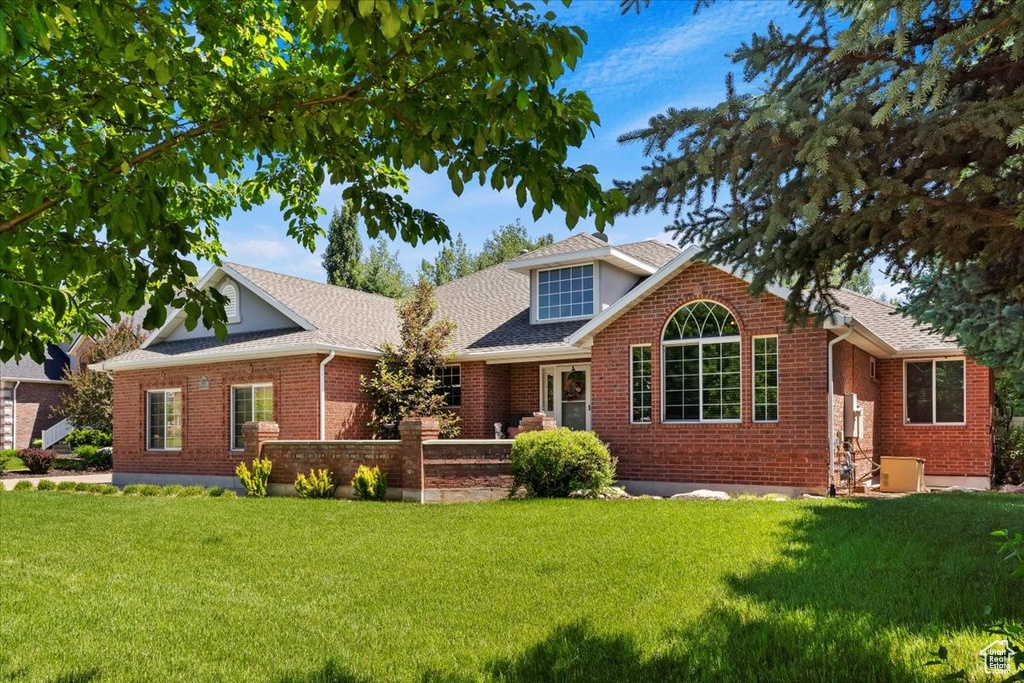 View of front facade with a front yard, brick siding, and roof with shingles