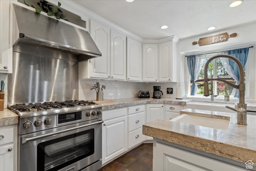 Kitchen with high end range, backsplash, white cabinetry, recessed lighting, and light stone counters