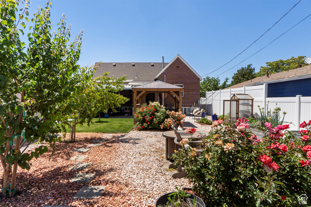 Rear view of house featuring a gazebo, a greenhouse, a patio, an outdoor structure, and brick siding