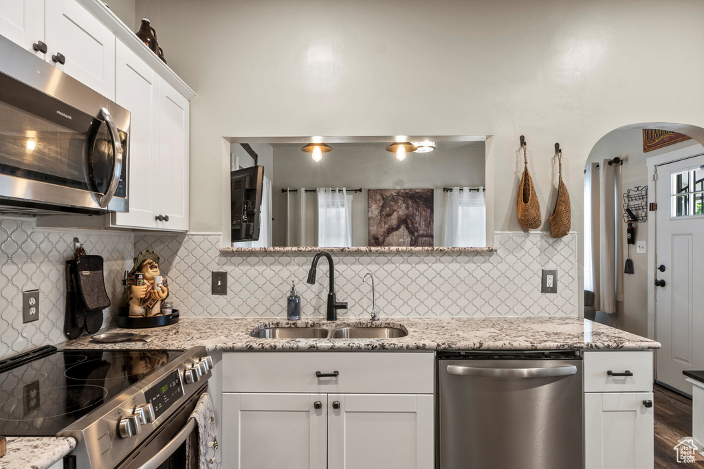 Kitchen featuring stainless steel appliances, arched walkways, white cabinetry, tasteful backsplash, and dark wood-type flooring