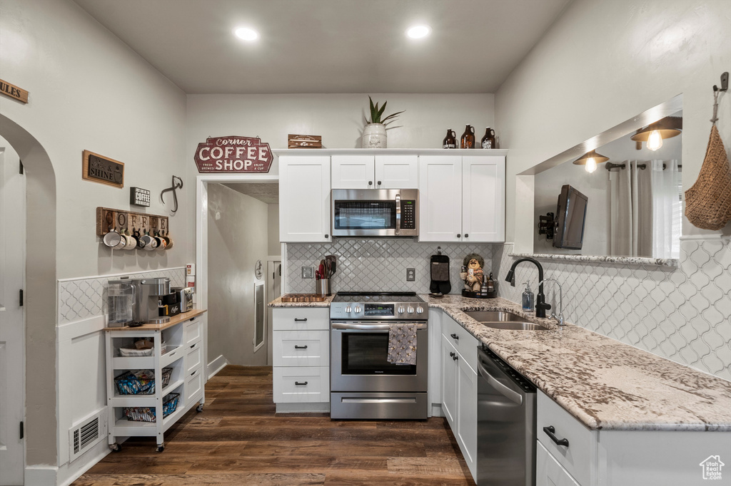 Kitchen featuring appliances with stainless steel finishes, tasteful backsplash, arched walkways, light stone counters, and white cabinets