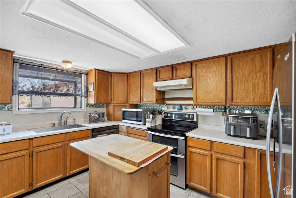Kitchen with appliances with stainless steel finishes, under cabinet range hood, butcher block counters, light tile patterned floors, and brown cabinetry