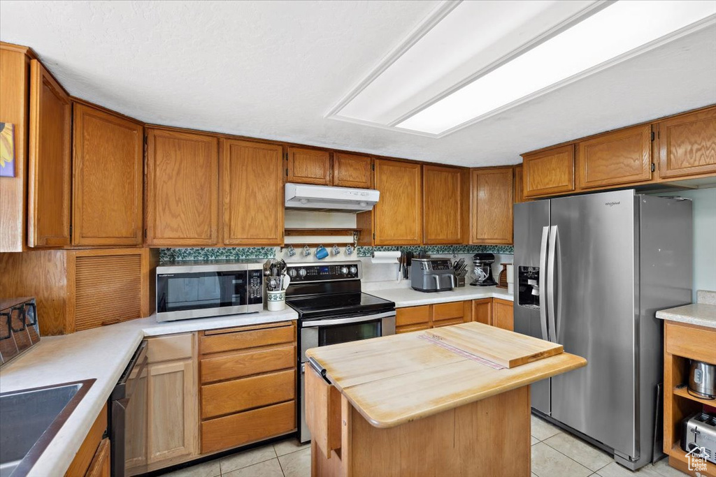 Kitchen with appliances with stainless steel finishes, under cabinet range hood, light tile patterned floors, and wood counters