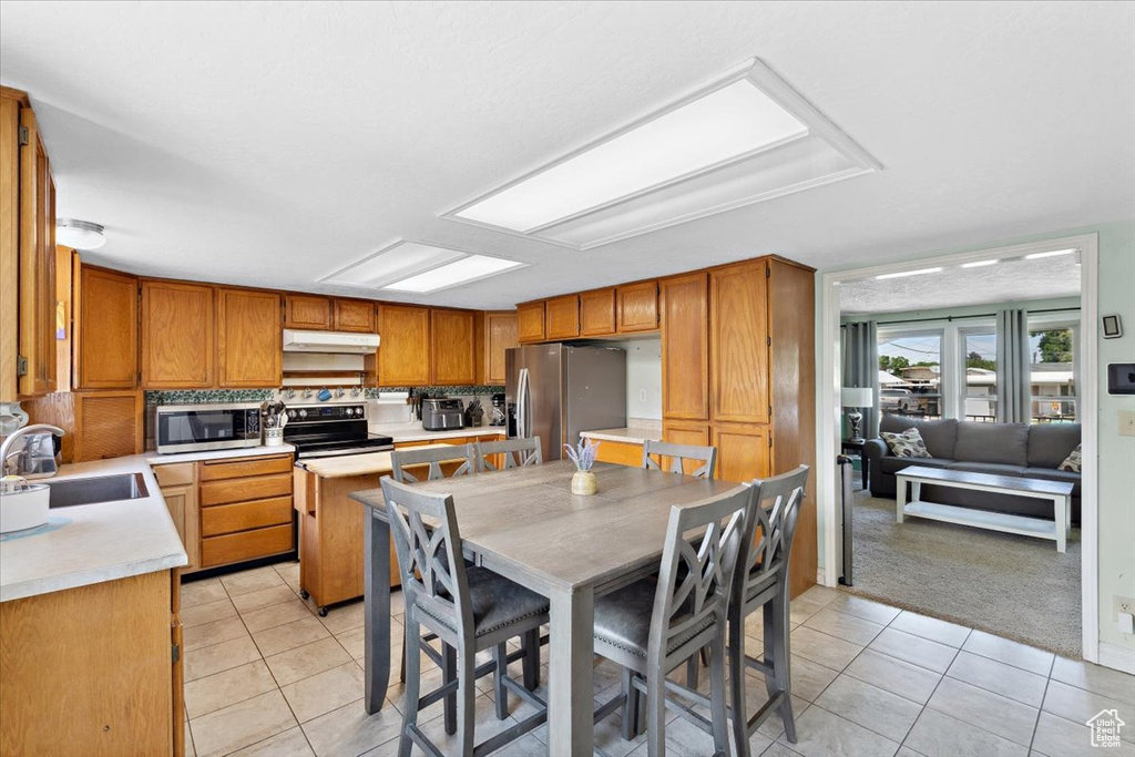 Kitchen with appliances with stainless steel finishes, light tile patterned floors, light countertops, under cabinet range hood, and brown cabinetry
