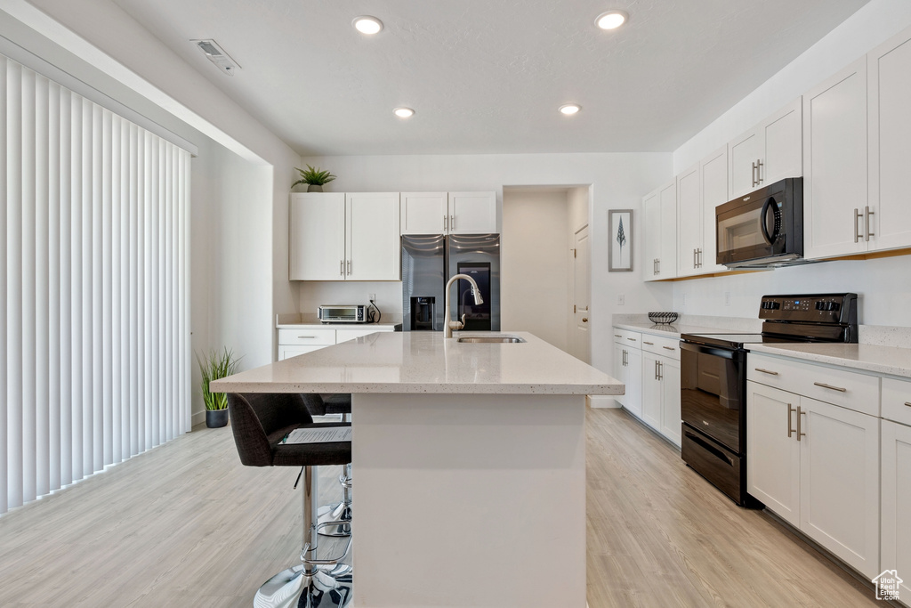 Kitchen with black appliances, a sink, light wood-type flooring, an island with sink, and recessed lighting