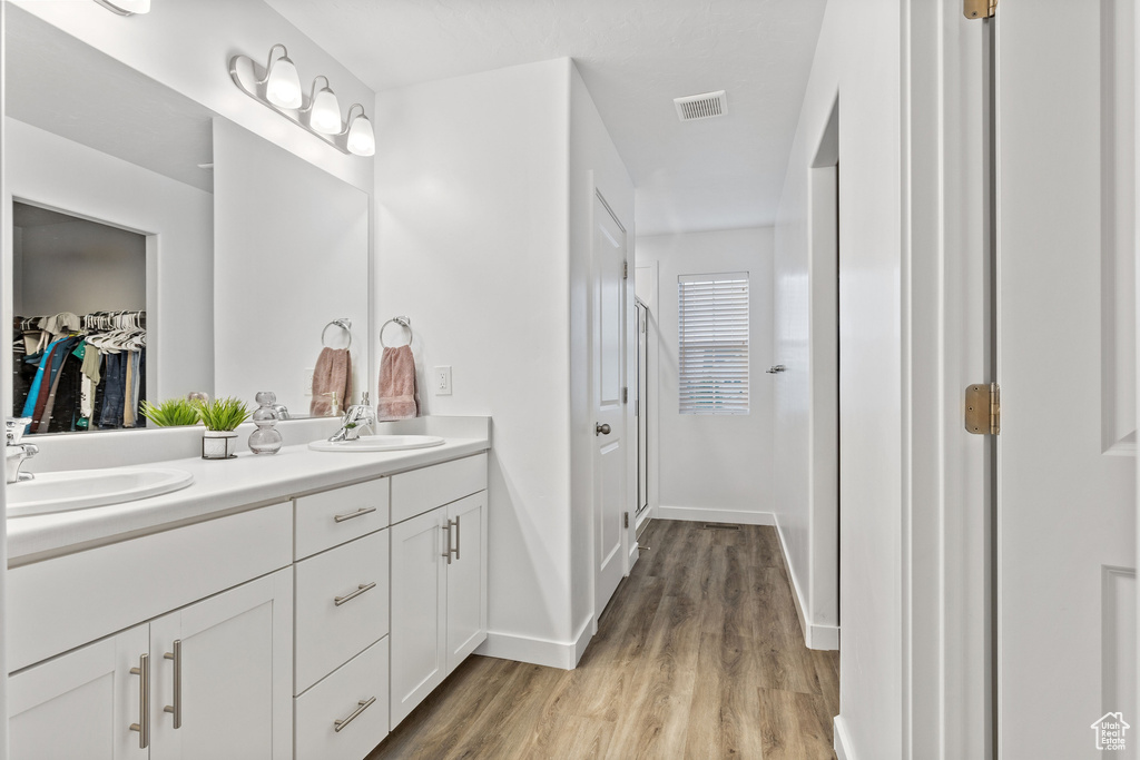Full bath with double vanity, wood finished floors, baseboards, and a walk in closet