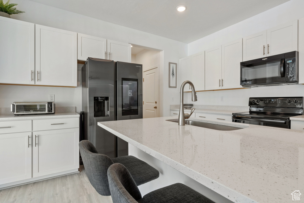 Kitchen with black appliances, white cabinets, light stone counters, a sink, and recessed lighting