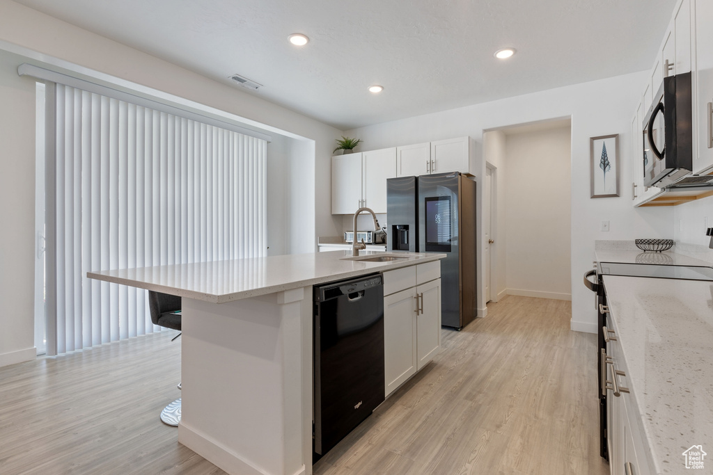 Kitchen with black appliances, light wood finished floors, white cabinets, an island with sink, and recessed lighting