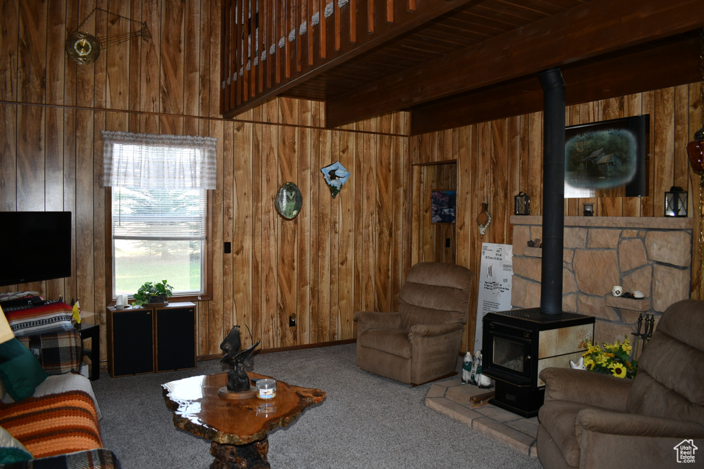 Carpeted living area featuring a wood stove, wood walls, and beamed ceiling