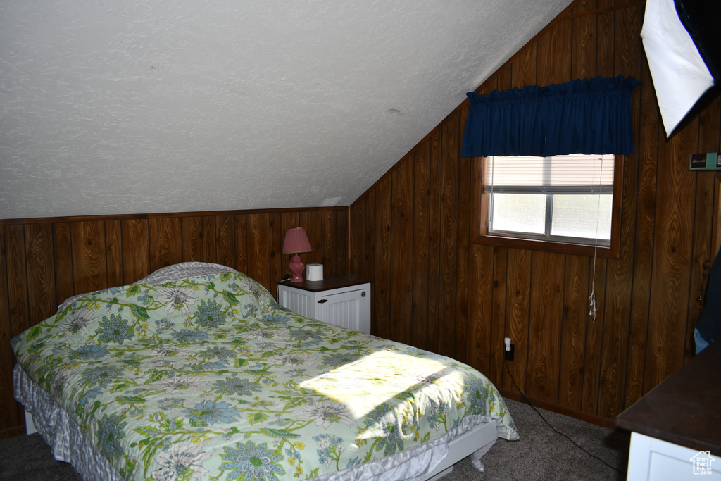 Bedroom with vaulted ceiling, wood walls, carpet flooring, and a textured ceiling