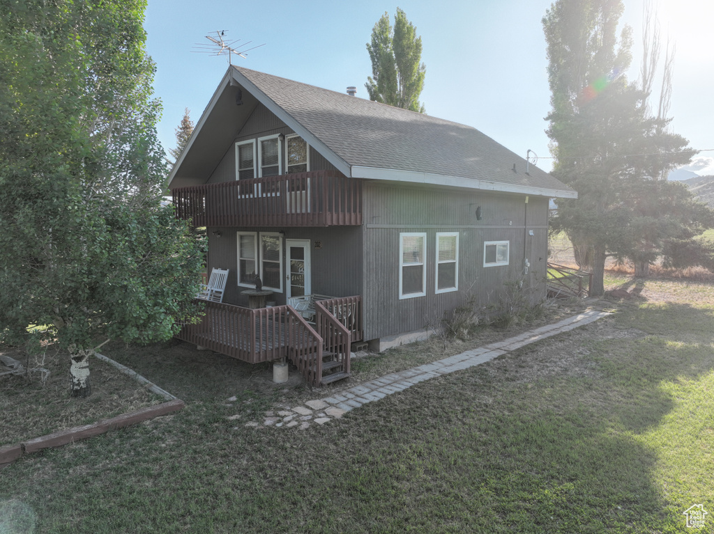 Back of property with a yard, a wooden deck, roof with shingles, and a balcony