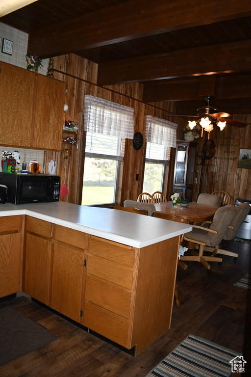 Kitchen with black microwave, wood walls, a peninsula, dark wood-style floors, and light countertops