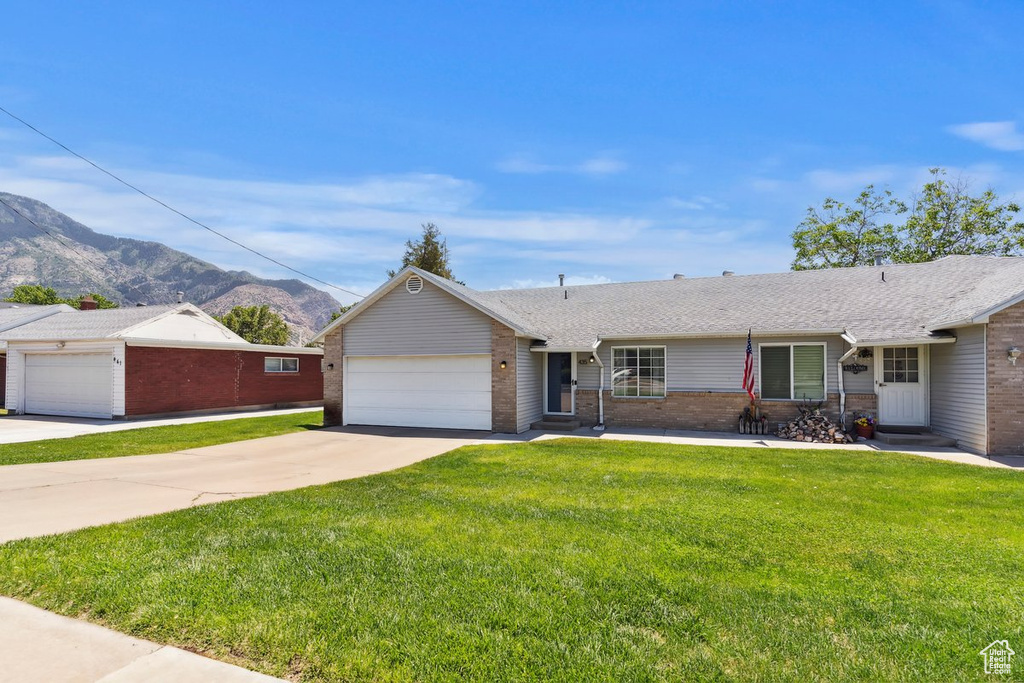 Single story home featuring brick siding, a garage, concrete driveway, a mountain view, and a front yard