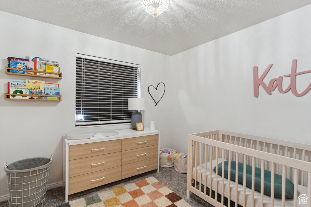 Bedroom with carpet, a textured ceiling, and a nursery area
