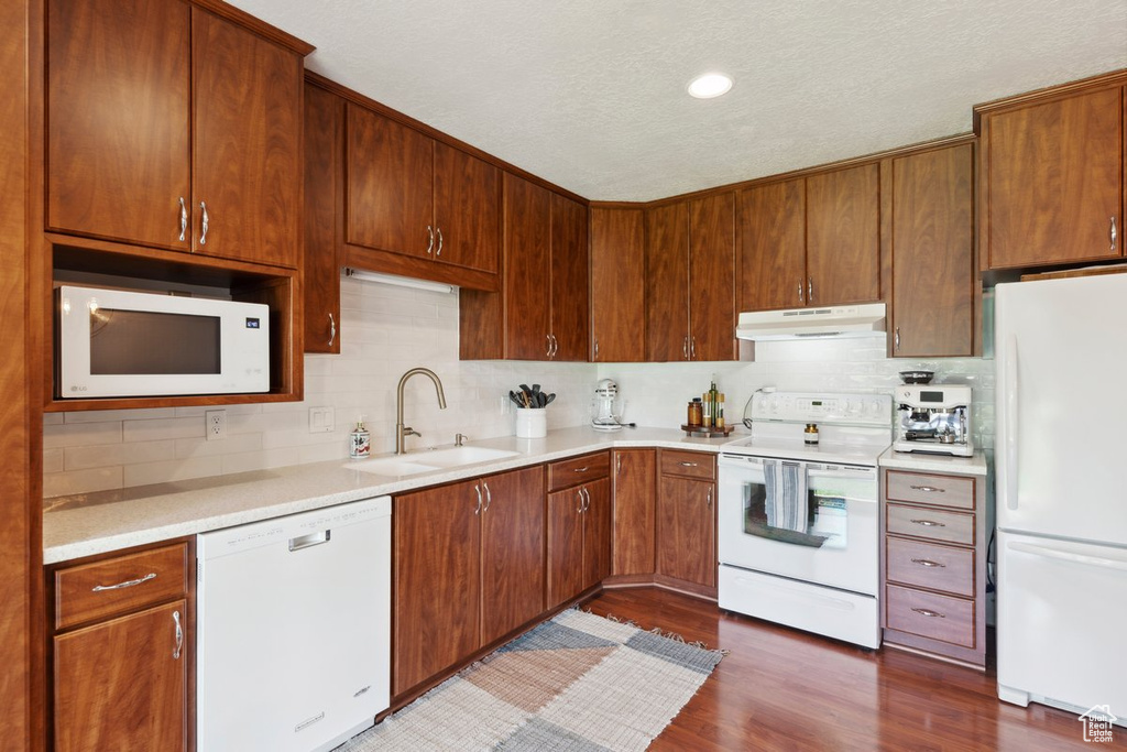 Kitchen featuring white appliances, under cabinet range hood, tasteful backsplash, light countertops, and dark wood finished floors