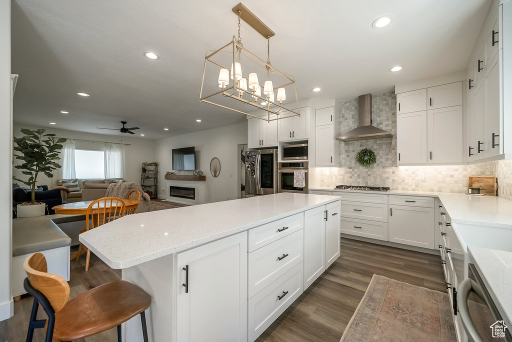 Kitchen with wall chimney exhaust hood, stainless steel appliances, a center island, white cabinetry, and recessed lighting