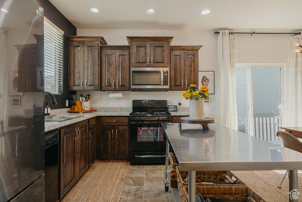 Kitchen with black appliances, dark brown cabinetry, recessed lighting, and light stone finish flooring