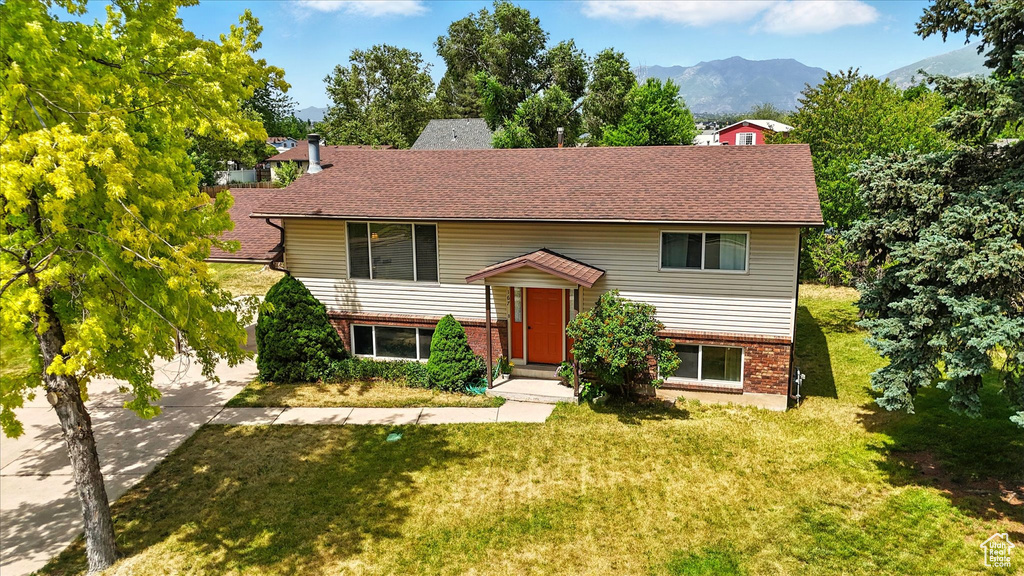 Split foyer home with brick siding, a front lawn, a mountain view, a shingled roof, and driveway