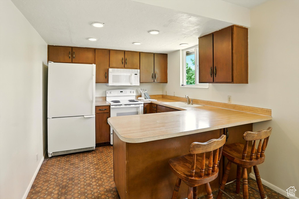Kitchen featuring white appliances, light countertops, a peninsula, brown cabinets, and a kitchen breakfast bar