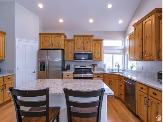 Kitchen featuring appliances with stainless steel finishes, lofted ceiling, light wood finished floors, a kitchen island, and light stone counters