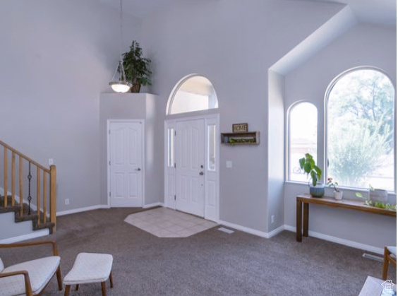 Carpeted foyer featuring healthy amount of natural light, stairway, and high vaulted ceiling