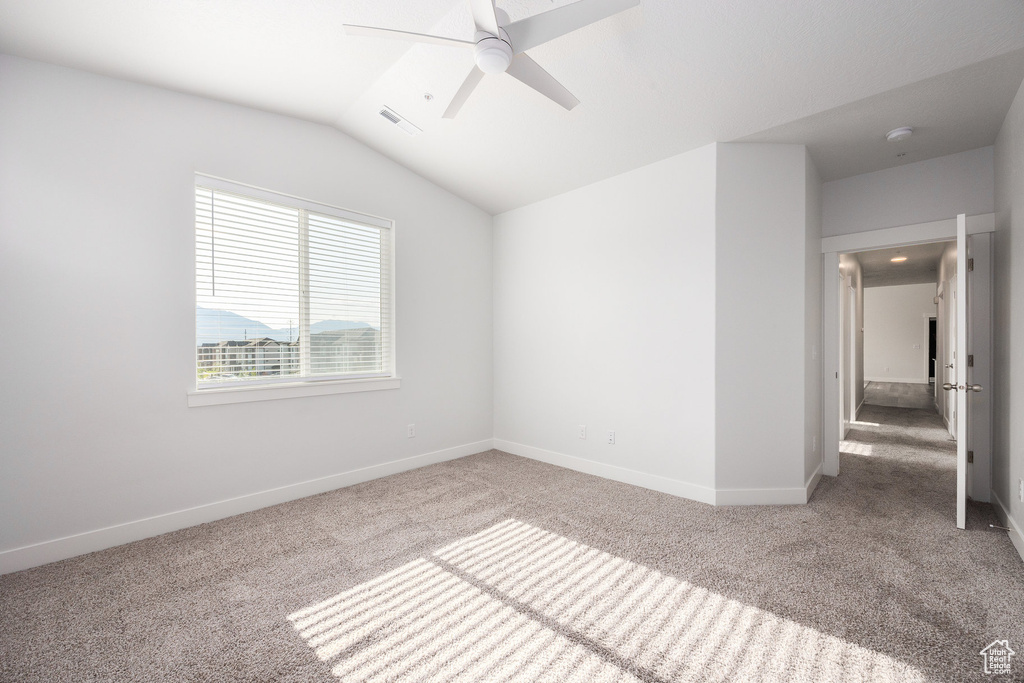 Empty room with carpet flooring, a ceiling fan, a smoke detector, and vaulted ceiling