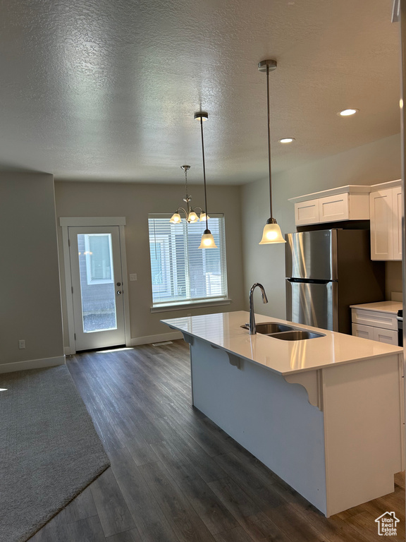 Kitchen featuring freestanding refrigerator, a sink, white cabinets, light countertops, and a chandelier
