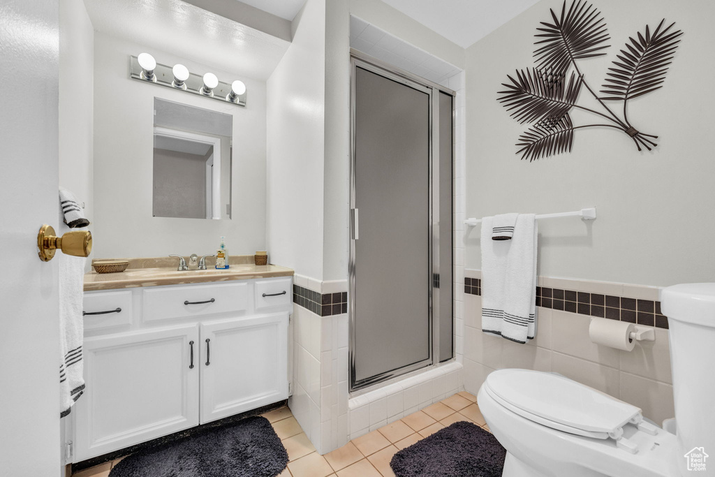 Bathroom with toilet, tile patterned floors, tile walls, vanity, and a shower stall