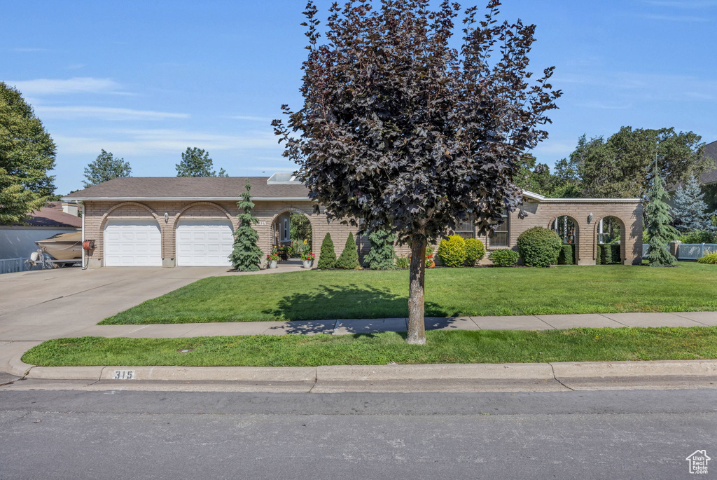 View of front of property with a front yard, driveway, brick siding, and an attached garage
