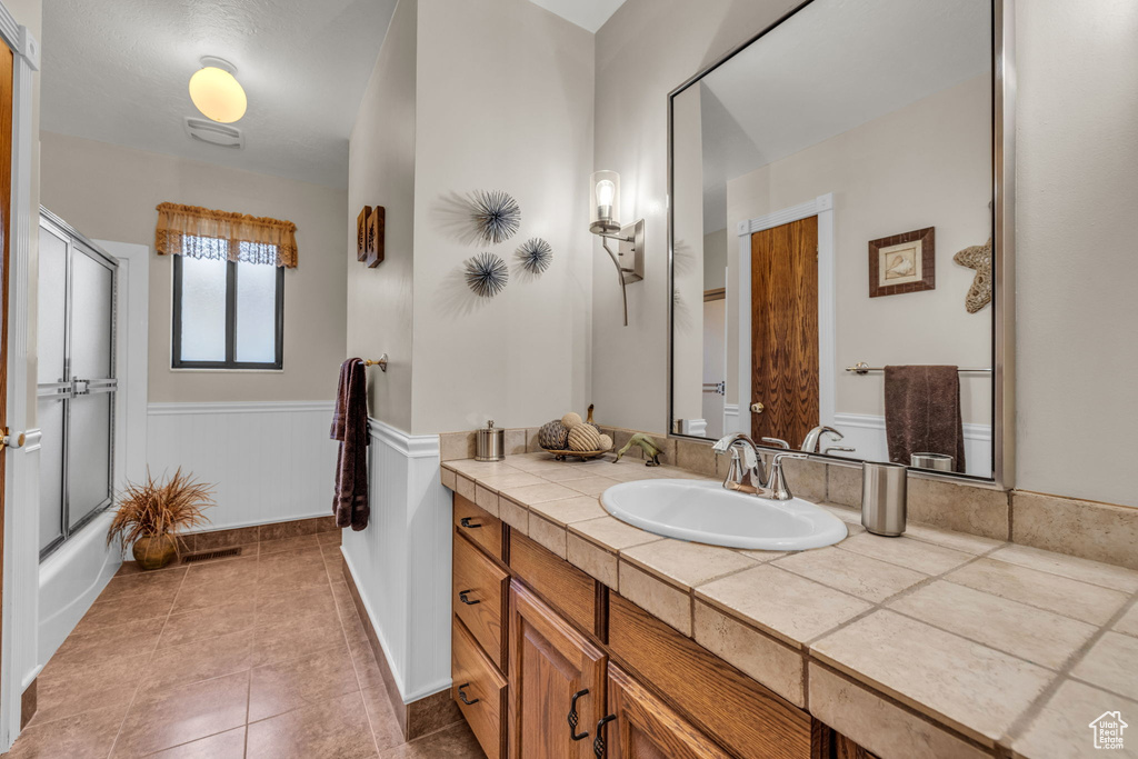 Full bathroom with vanity, a wainscoted wall, tile patterned flooring, and enclosed tub / shower combo