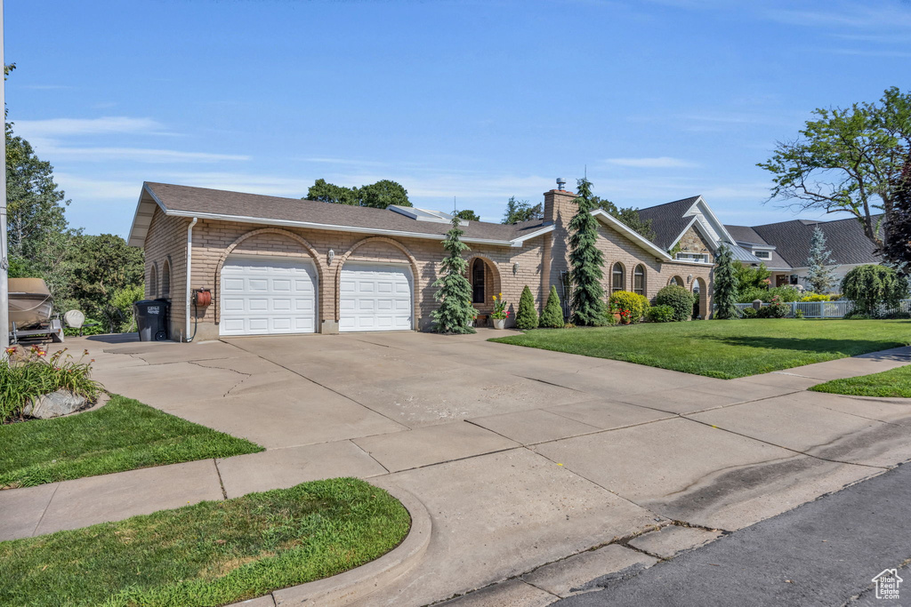 View of front of home with an attached garage, driveway, a front lawn, and brick siding