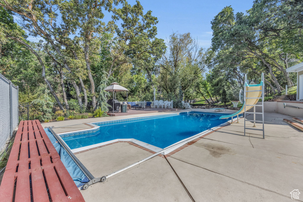 Swimming pool featuring a patio area, a water slide, and view of scattered trees