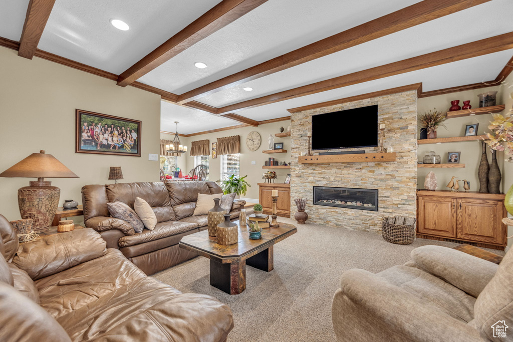 Living room featuring beam ceiling, a chandelier, ornamental molding, carpet, and a stone fireplace
