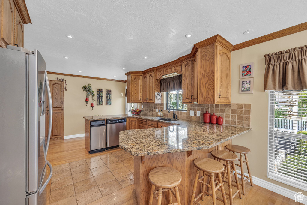 Kitchen featuring appliances with stainless steel finishes, a peninsula, baseboards, backsplash, and a sink