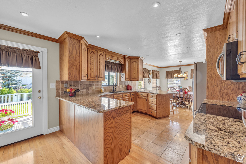 Kitchen featuring a peninsula, appliances with stainless steel finishes, a sink, a chandelier, and backsplash