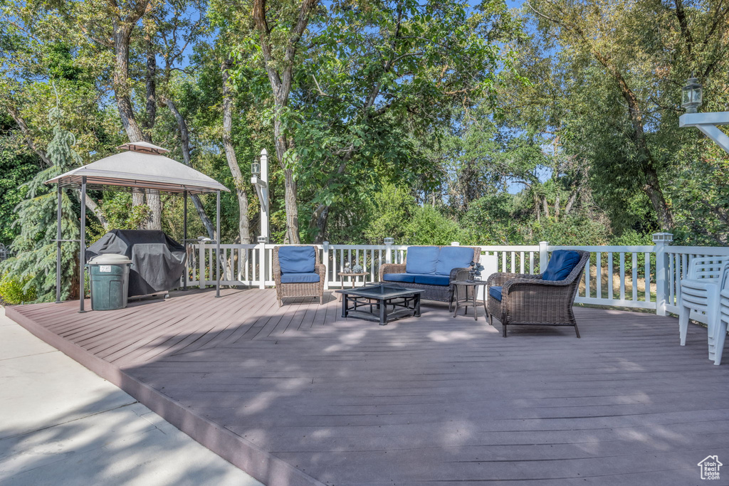 Wooden deck with an outdoor hangout area, area for grilling, a gazebo, and view of scattered trees