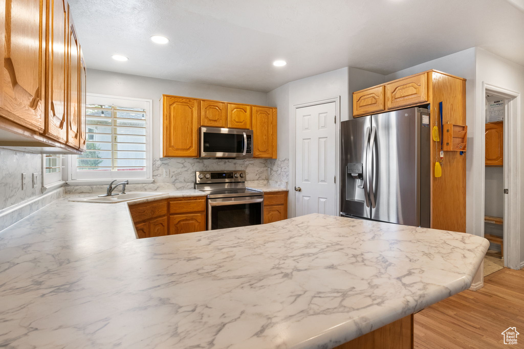 Kitchen with stainless steel appliances, a peninsula, decorative backsplash, light countertops, and recessed lighting