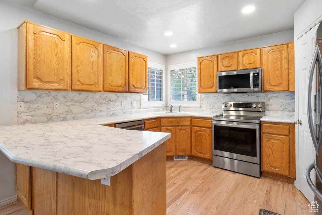 Kitchen featuring appliances with stainless steel finishes, a peninsula, decorative backsplash, light wood-type flooring, and recessed lighting