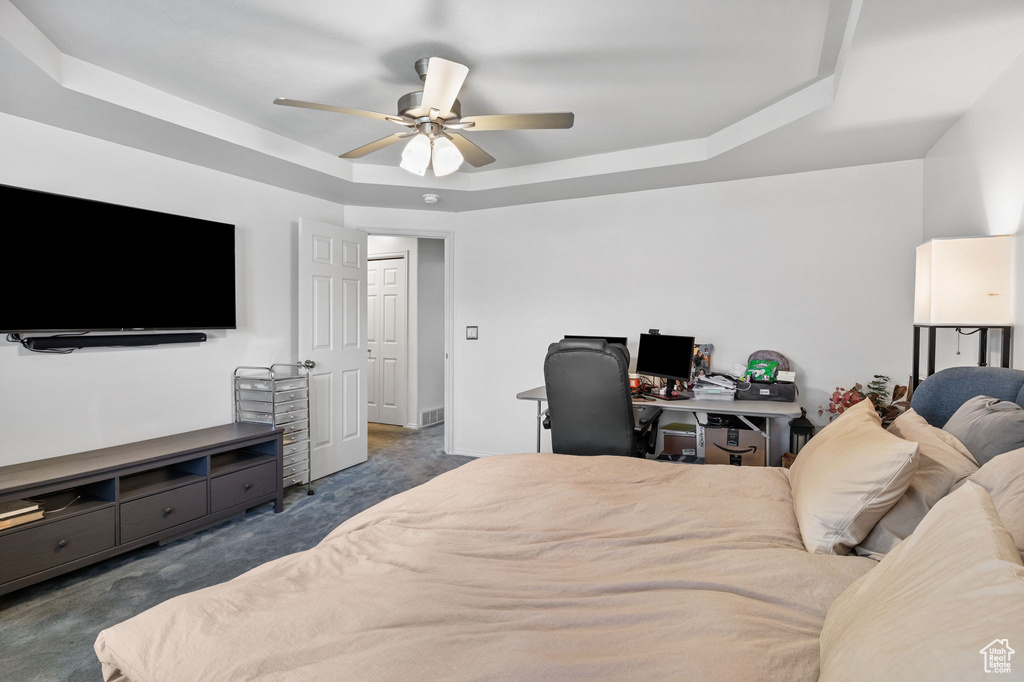 Carpeted bedroom with a raised ceiling, ceiling fan, and a desk