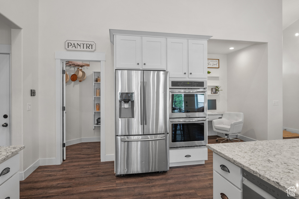 Kitchen with stainless steel appliances, dark wood-style flooring, white cabinetry, light stone counters, and recessed lighting