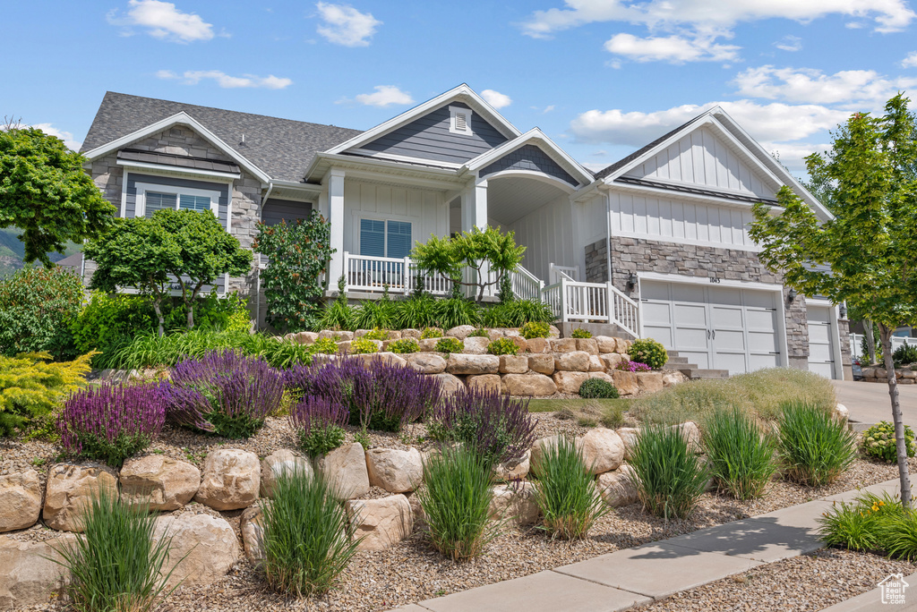 View of front of property featuring stone siding, covered porch, board and batten siding, concrete driveway, and a garage