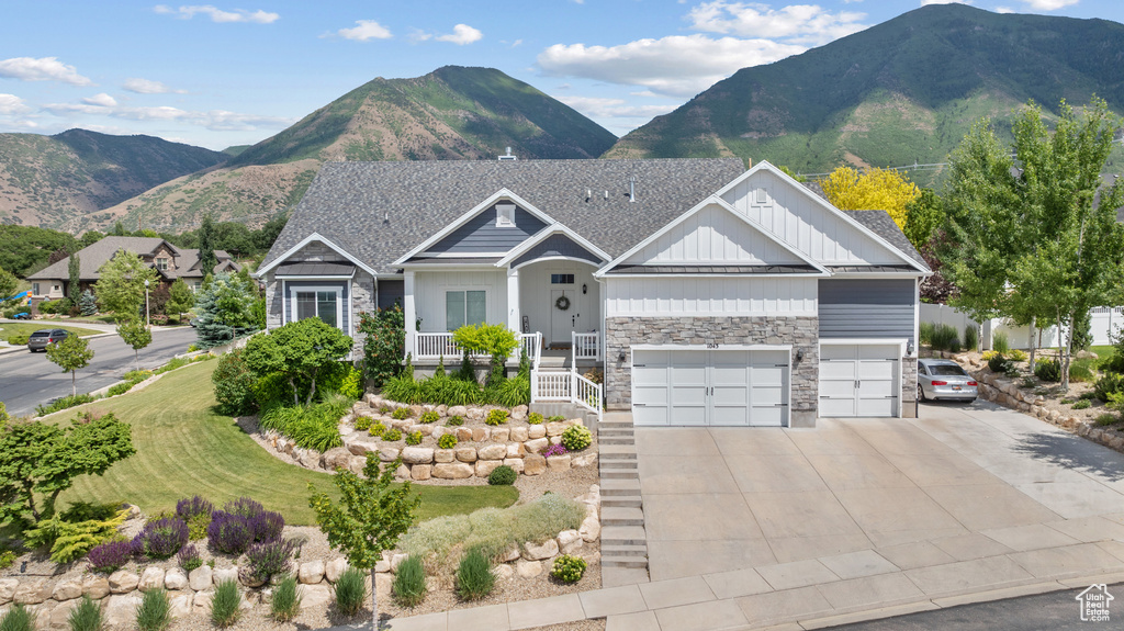 Craftsman house with board and batten siding, stone siding, concrete driveway, an attached garage, and a mountain view